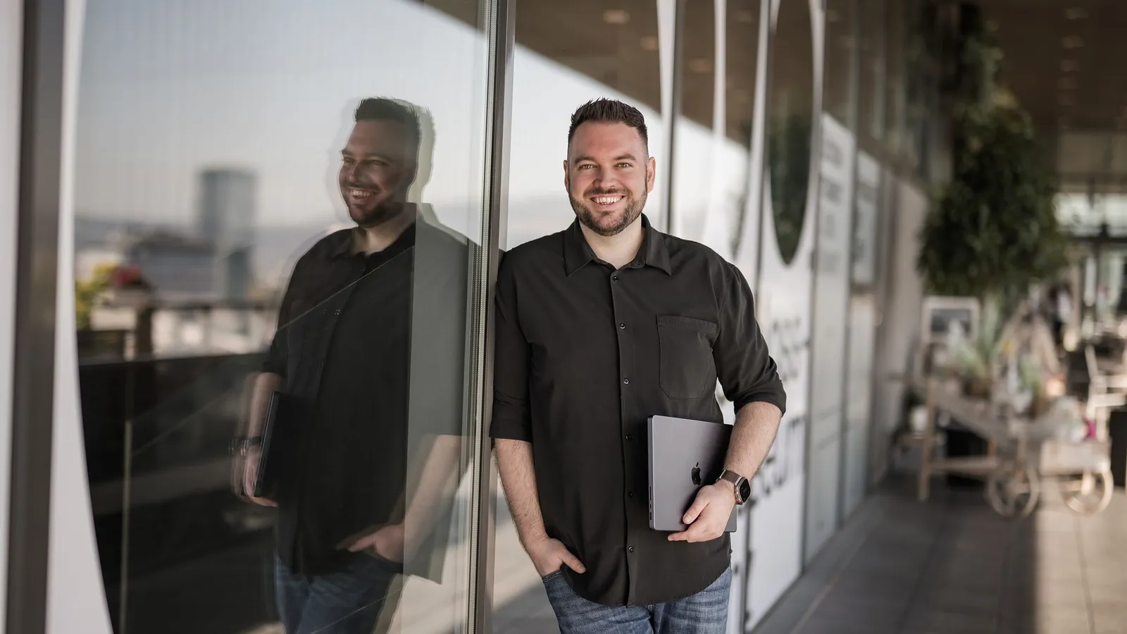 Philipp Unterholzer lehnt mit MacBook an der Glasfront des Schlossmuseums Linz