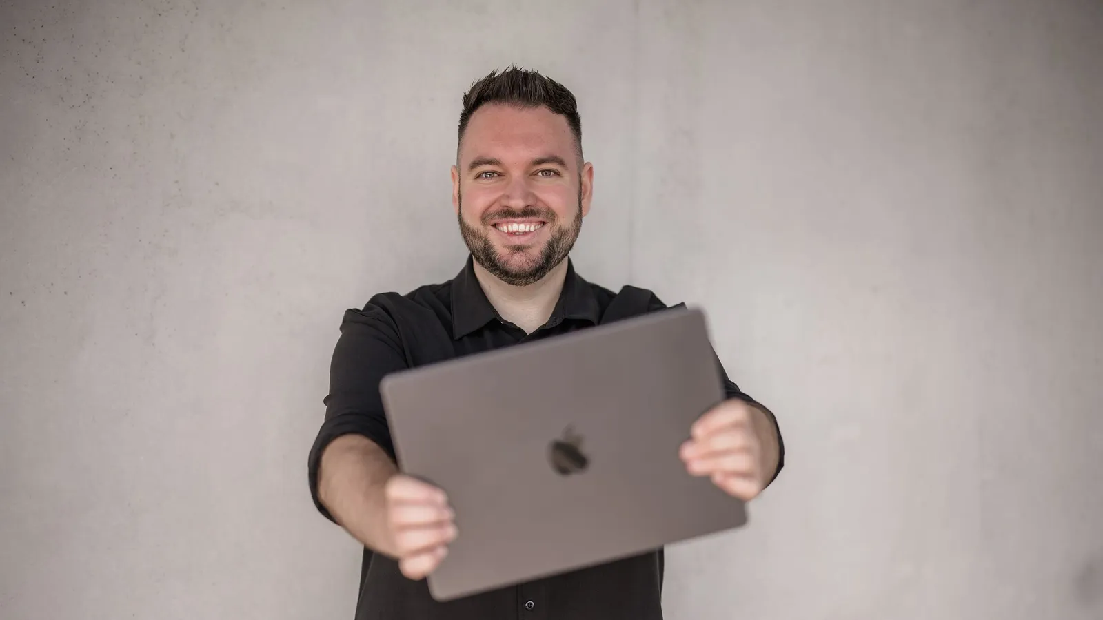 Philipp Unterholzer hält lächelnd ein MacBook in die Kamera